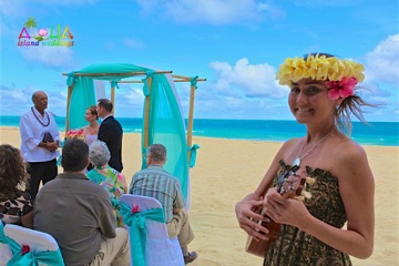 Jena playing the ukulele and wearing a flower haku lei at a beach wedding
